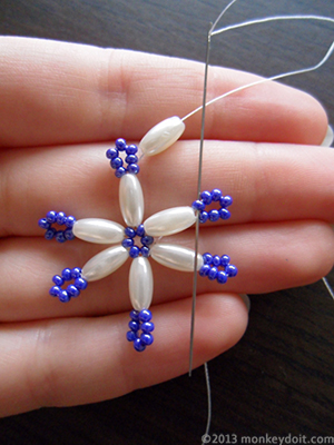 String an oval bead onto the thread and push the needle down through one seed bead from the neighbouring ‘arm’ of the snowflake