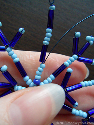 When you complete the last short arm, push the wire up the very first long arm you created until you come out just below the first bugle bead