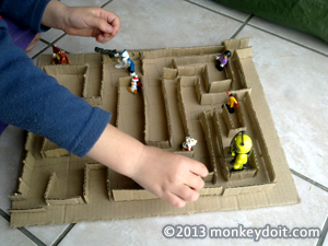 Child playing with cardboard maze with figurines